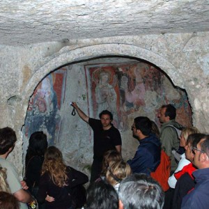 sei-su-immagine-raffigurante-Francesco-mentre-spiega-l-affresco-riproducente-la-Madonna-del-Melograno-nella-chiesa-rupestre-della-madonna-delle-tre-porte